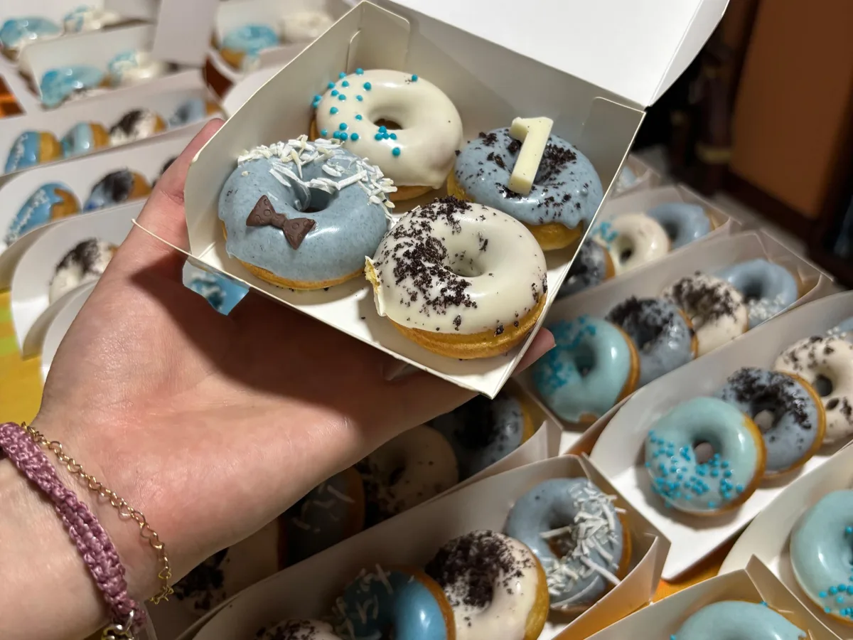 Caja abierta con minidonas decoradas sostenida frente a más cajas.